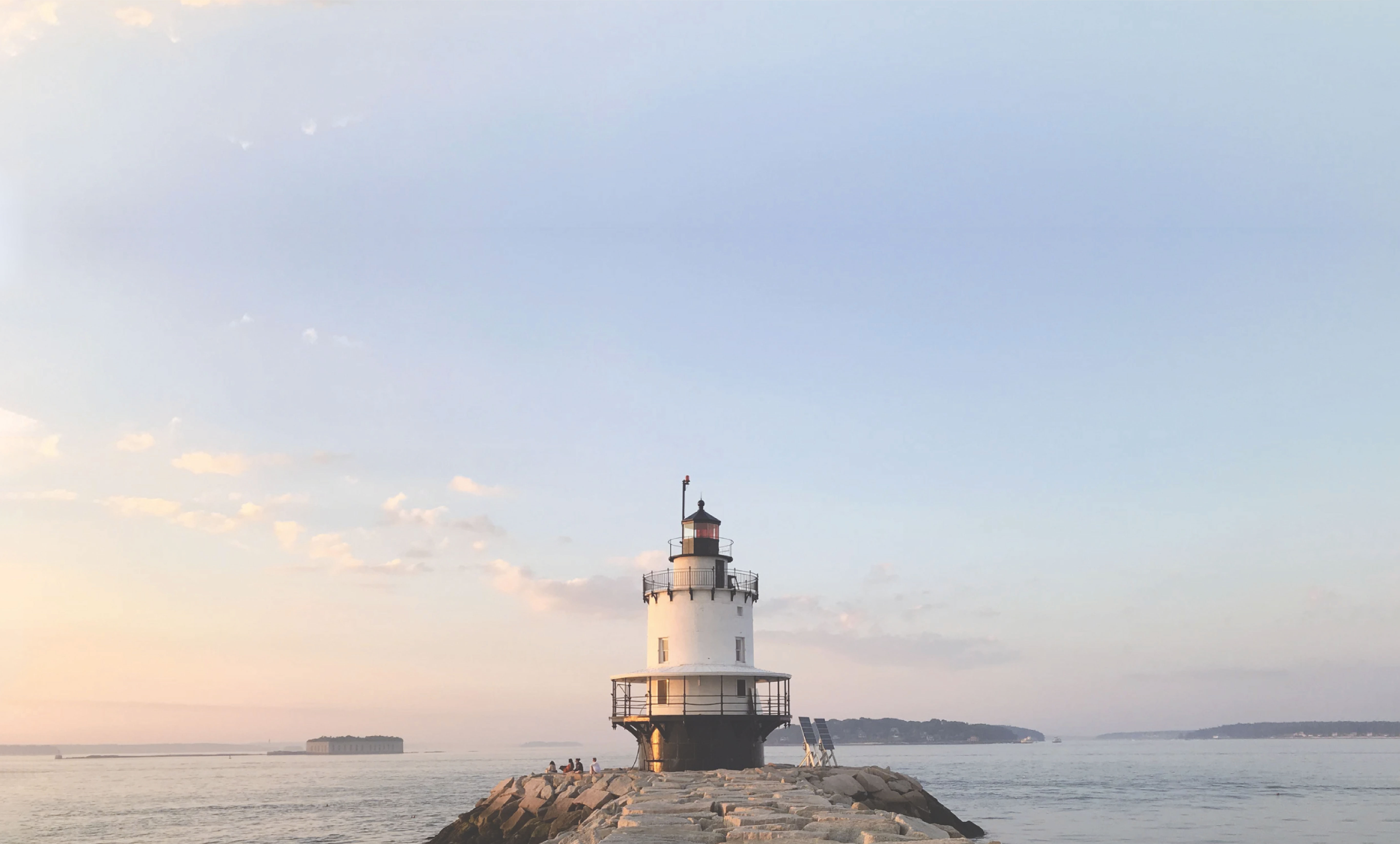 A lighthouse on a rock in portland, maine with sunset behind it.